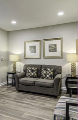 A living room with a couch, chair, and coffee table. A lamp is on the table. A mirror is on the wall. A painting is on the wall. A doorway is in the room. AI generated content